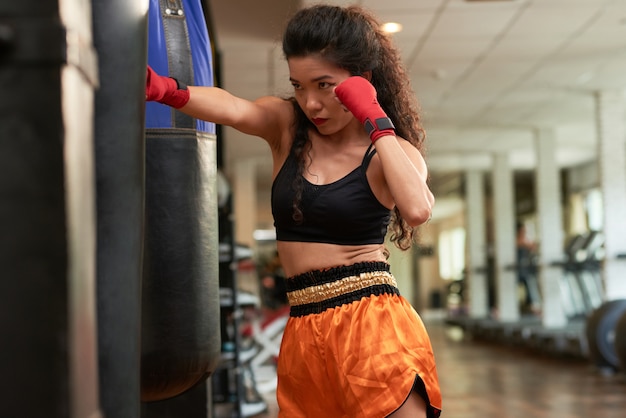 Boxer féminin pratiquant des coups de poing sur un sac de boxe dans un gymnase