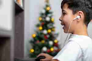 Photo gratuite boy utilise un pc avec des écouteurs. sapin de noël sur le mur. visage heureux et excité