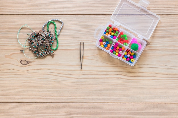 Photo gratuite bracelet; pince à épiler et boîte de perles colorées sur la table