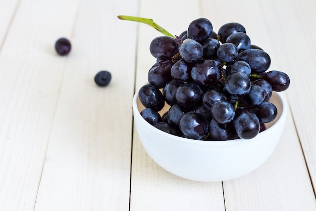 Branche de raisin noir dans un bol en bois blanc