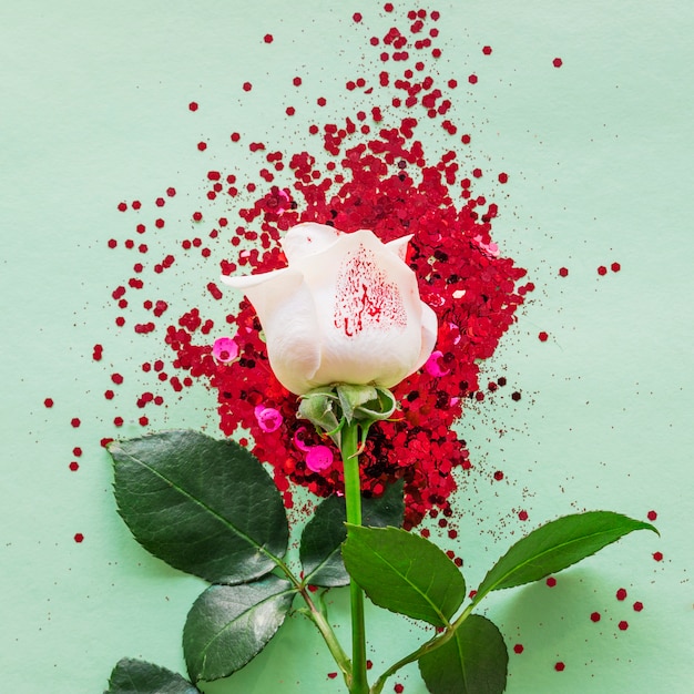 Photo gratuite branche de rose blanche avec des paillettes sur la table