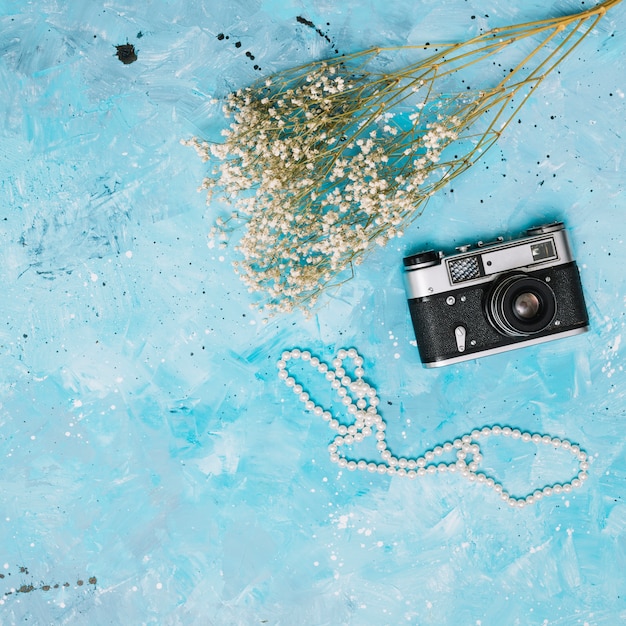 Photo gratuite branches de fleurs avec caméra et perles sur table