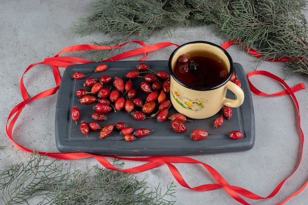 Photo gratuite branches de pin naturel à côté d'un plateau marine de cynorrhodons et d'une tasse de thé à l'églantier entouré de rubans sur une surface en marbre