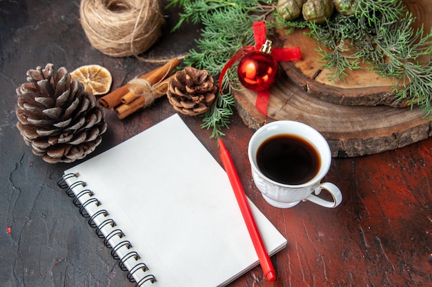 Branches de sapin et cahier à spirale fermé avec cône de conifère de limes à la cannelle et une tasse de thé noir sur fond sombre