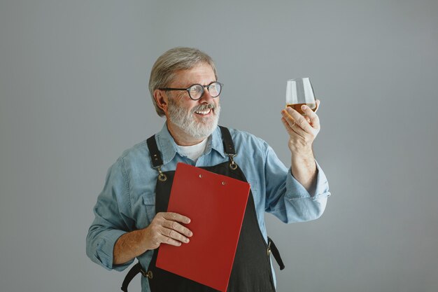 Brasseur d'homme senior confiant avec bière artisanale en verre sur tonneau en bois sur fond gris