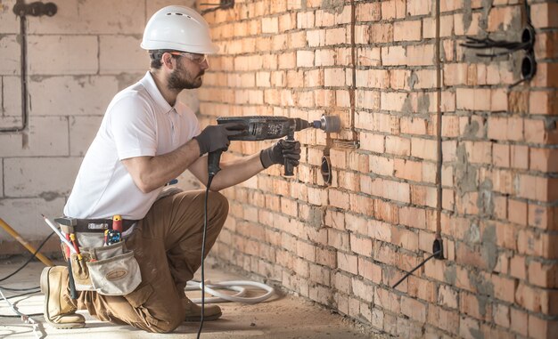 Le bricoleur utilise un marteau-piqueur, pour l'installation, un travailleur professionnel sur le chantier. Le concept d'électricien et de bricoleur.