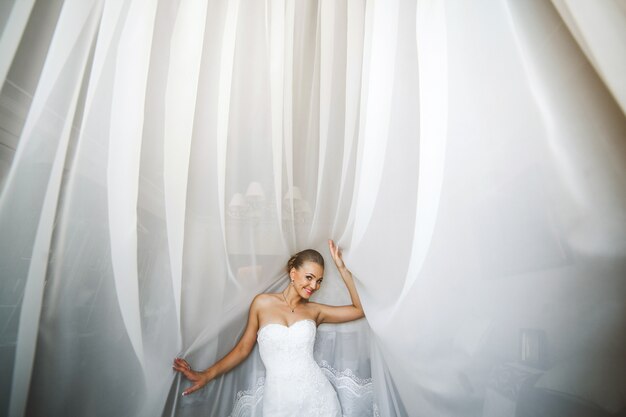 Bride posant avec des rideaux blancs