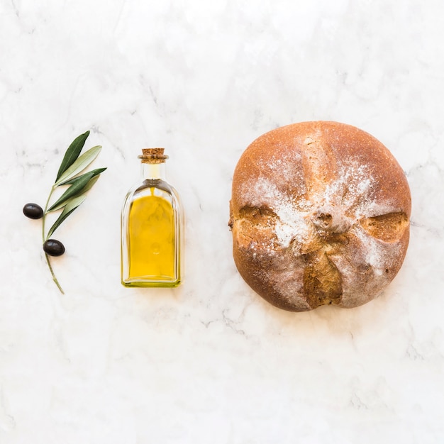 Photo gratuite brindille olive noire avec bouteille d'huile et chignon rond sur fond de marbre blanc