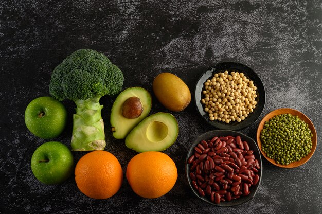 Brocoli, pomme, orange, kiwi, légumineuses et avocat sur un sol en ciment noir.