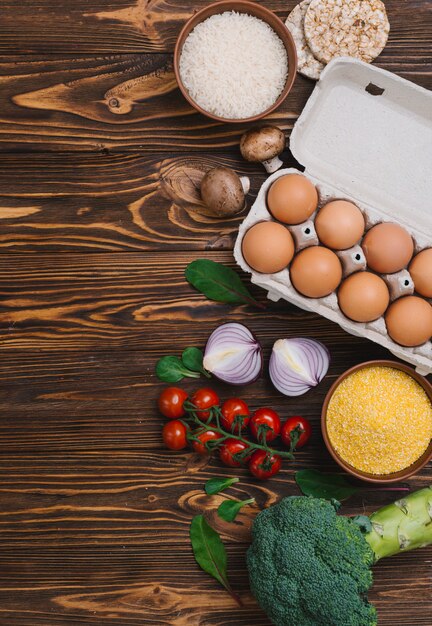 Brocoli; tomates cerises; oignon coupé en deux; champignon; gâteau de riz soufflé croustillant et bol de polenta sur le bureau en bois