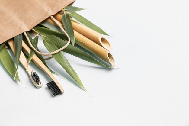 Brosse à dents en bambou et sac écologique sur une table avec espace de copie sur fond blanc Composition stylisée de mise à plat avec des feuilles de bambou
