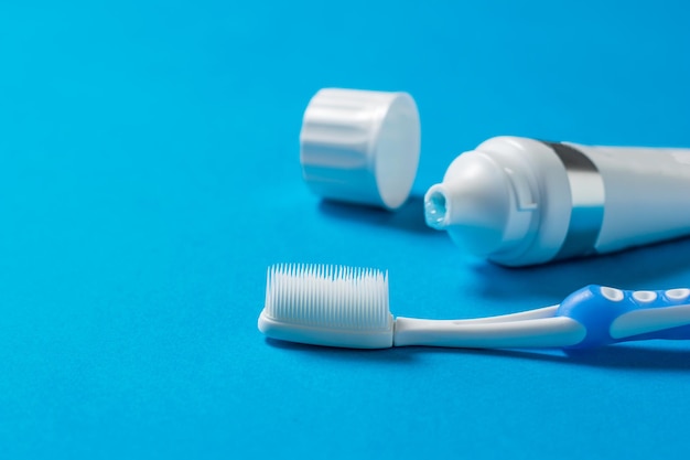 Une brosse à dents avec des poils en silicone et un tube de dentifrice sur fond bleu. moyens de prendre soin de la cavité buccale.