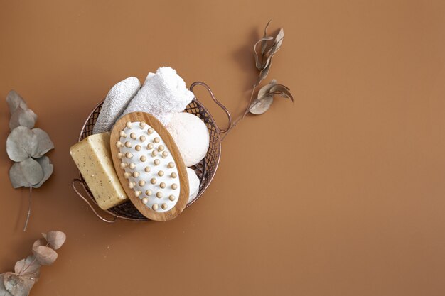 Brosse de massage, bombes de bain, savon et serviette dans le panier sur la vue de dessus de fond brun.