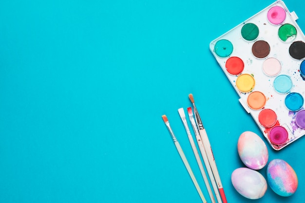 Des brosses; oeufs de Pâques peints et palette en plastique avec la couleur de l&#39;eau sur fond bleu