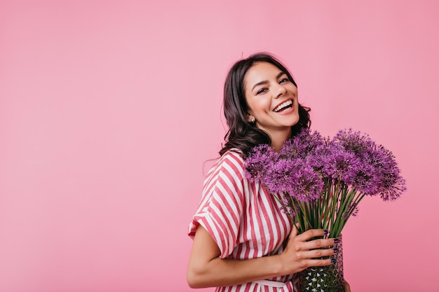 Une brune positive avec des fossettes rayonne de joie. Instantané de jolie dame frisée avec de belles fleurs violettes énormes.