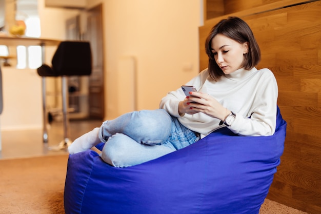 Photo gratuite une brune sexy est assise dans une chaise de sac violet vif en utilisant son téléphone pour envoyer des sms avec ses amis