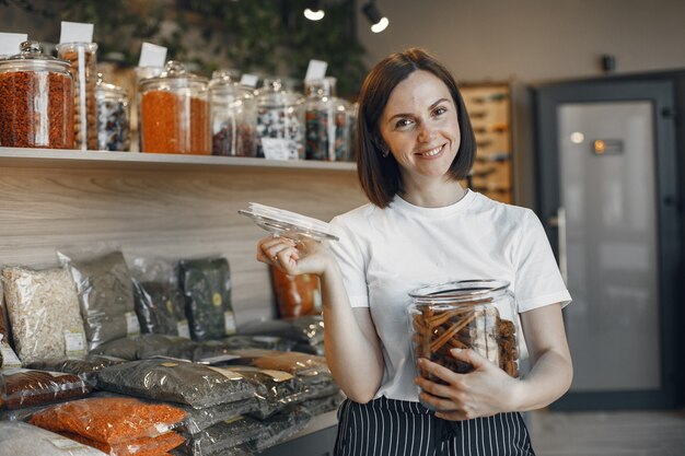 Brunette choisit la nourriture. Dame tenant un pot de cannelle. Fille dans une chemise blanche au supermarché.