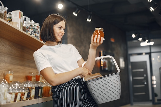 Brunette choisit la nourriture. Dame tient un caddie Fille dans une chemise blanche dans le supermarché.