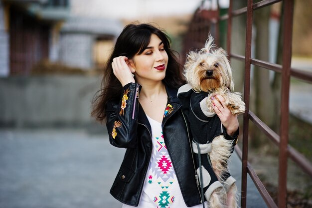 Brunette gitane avec chien yorkshire terrier posé contre des garde-corps en acier Modèle porter sur une veste en cuir et un t-shirt avec un pantalon d'ornement