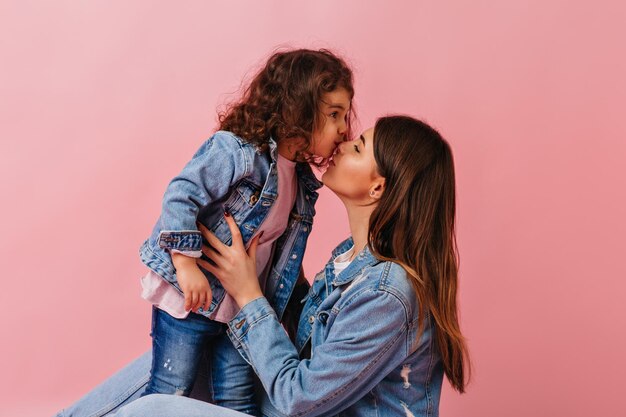 Brunette jeune maman embrassant un enfant Studio photo d'une préadolescente aux cheveux noirs exprimant l'amour à sa mère