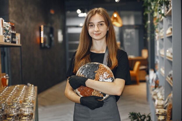 Brunette regarde la caméra et sourit. Femme en tablier. Dame dans le magasin.