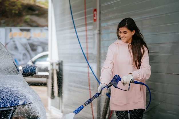 Brunette d'un tuyau à haute pression applique un nettoyant sur la voiture