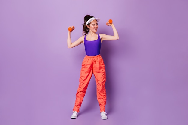 Brunette woman in cap est engagée dans la remise en forme sur le mur violet