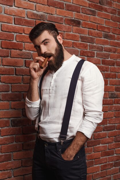 Brutal jeune bel homme fumant le cigare sur le mur de briques.