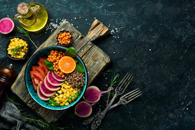 Buddha bowl : quinoa, épinards, maïs, tomates et radis pastèque, argousier. manger végétarien sain, super nourriture. vue de dessus sur un fond de pierre.