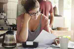 Photo gratuite budget et finances de la famille. femme sérieuse faisant des comptes et se sentant frustrée par le montant des dépenses mensuelles. jeune femme portant des lunettes calcul des factures de services publics, assis à la table de la cuisine