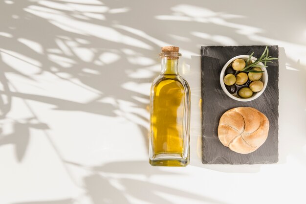 Bun et olives dans un bol avec une bouteille d&#39;huile sur l&#39;ombre tombant sur le fond blanc