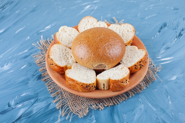 Bun et pain de mie sur une assiette sur une serviette en toile de jute sur fond bleu.