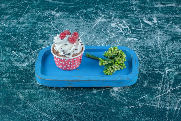 Bundle de boutons floraux et un petit gâteau sur un plateau en bois sur fond bleu. Photo de haute qualité