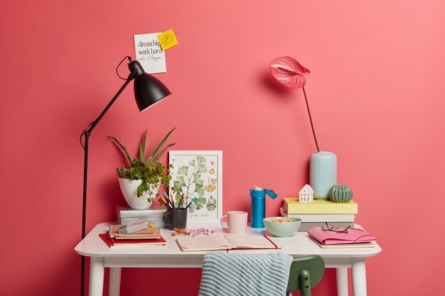 Bureau blanc d'étudiant avec lampe, cahier ouvert, livres, thermos de café et de lis calla roses dans un vase