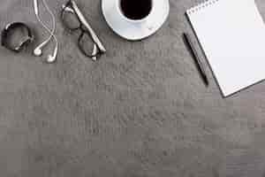 Photo gratuite bureau gris avec écouteur; lunettes; montre-bracelet; tasse à café; stylo et bloc-notes spirale vierge