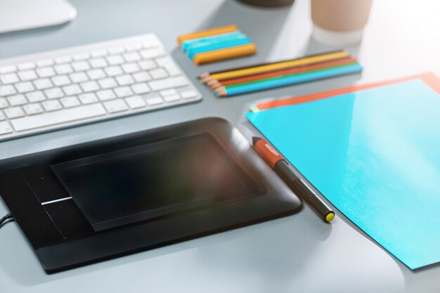 Le bureau gris avec ordinateur portable, bloc-notes avec feuille vierge, pot de fleur, stylet et tablette pour les retouches