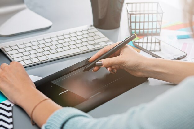 Le bureau gris avec ordinateur portable, bloc-notes avec feuille vierge, pot de fleur, stylet et tablette pour les retouches