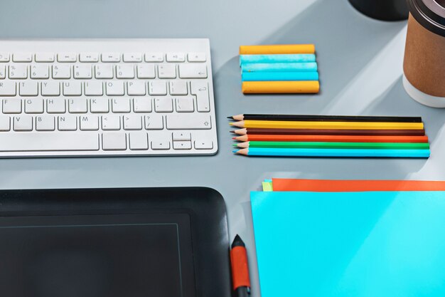 Le bureau gris avec ordinateur portable, bloc-notes avec feuille vierge, pot de fleur, stylet et tablette pour les retouches