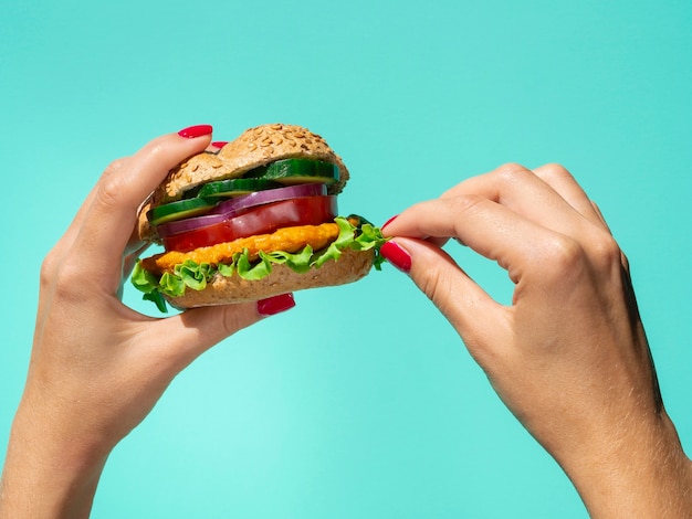 Burger de légumes tenu dans la main sur un fond bleu