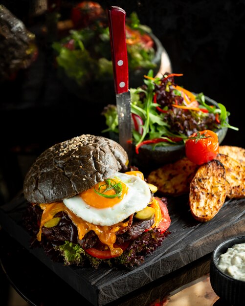 Burger en petit pain noir avec oeuf au plat et pommes de terre.