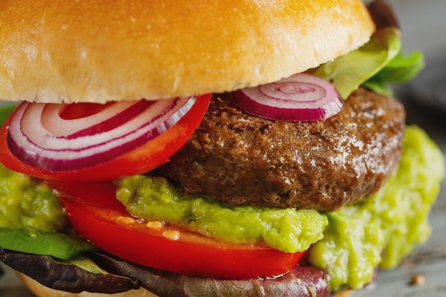 Burger à la viande et sauce avocat servi sur table en bois. Fermer.