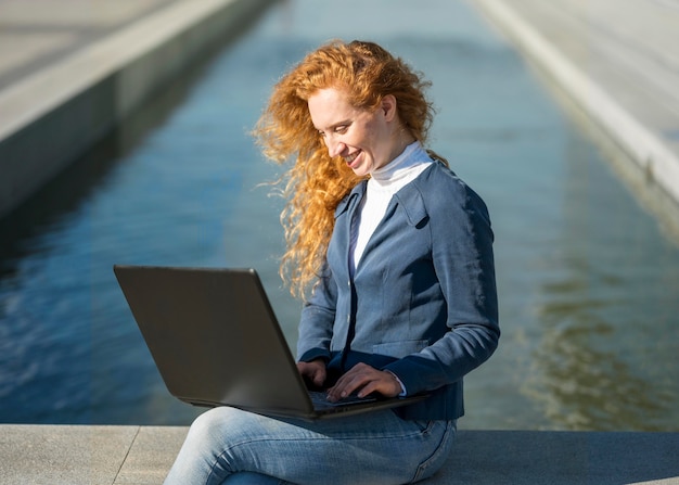 Photo gratuite businesswoman assis à côté d'une rivière et travaillant