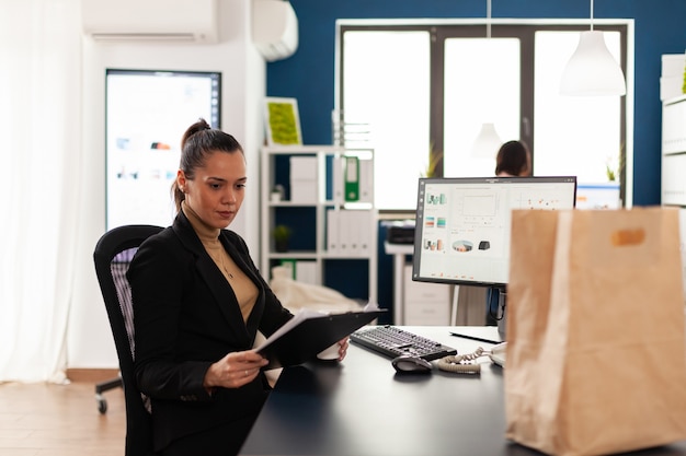 Businesswoman in corporate start up office analysant des documents, graphique en regardant le presse-papiers