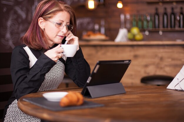Businesswoman looking at tablet tout en parlant avoir une conversation sur son téléphone. Travailler dans un café vintage