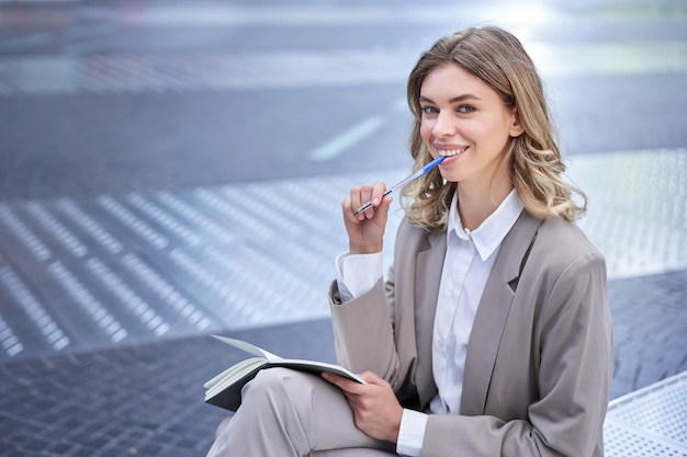 Businesswoman sitting in city centre with notebook and pen corporate woman écrit des idées thinki