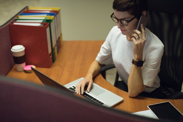 Businesswoman talking on mobile phone tout en utilisant un ordinateur portable au bureau