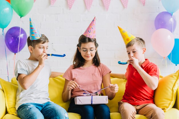 Cadeau d&#39;anniversaire déballage fille pendant que ses amis soufflant corne de fête