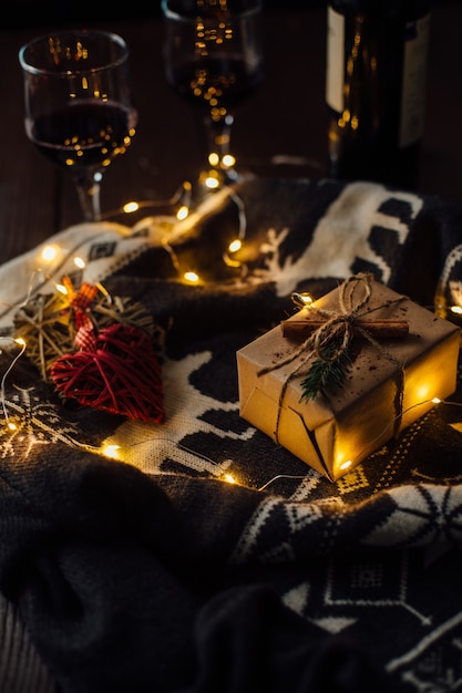 Cadeau de Noël avec chandail tricoté, lumières de Noël et deux verres de vin.