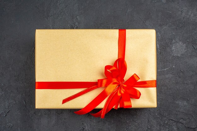 Cadeau de Noël vue de dessus en papier brun attaché avec un ruban rouge sur une surface sombre