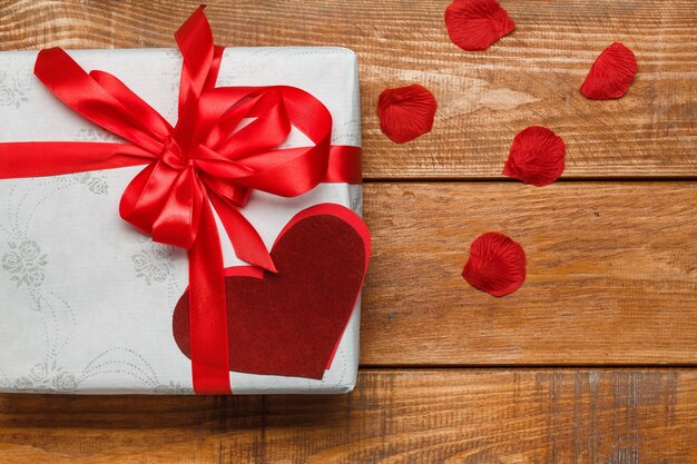 Cadeau de Saint Valentin dans une boîte blanche et coeurs et pétales sur fond de bois